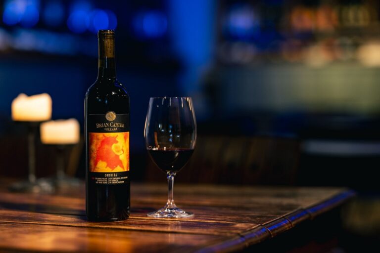 Brian Carter Cellars Corrida wine bottle and glass on a wooden table with candles in a dimly lit setting.