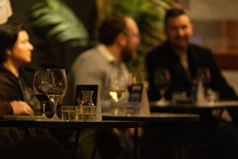 People enjoying drinks and conversation at a dimly lit event with tables set with wine glasses and decor.