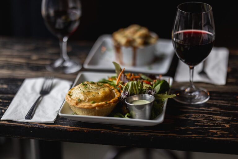 Savory pie with salad and red wine on a rustic wooden table, creating an inviting dining setting.