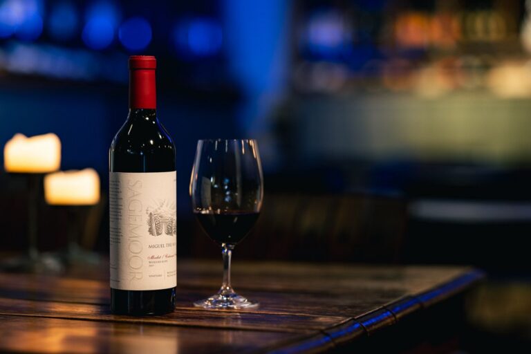Sagemoor Estates wine bottle and glass on wooden table with candles in dimly lit setting.