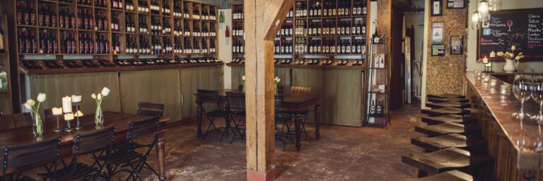 Cozy winery tasting room with wooden decor, wine bottles displayed on shelves, and seating for visitors.