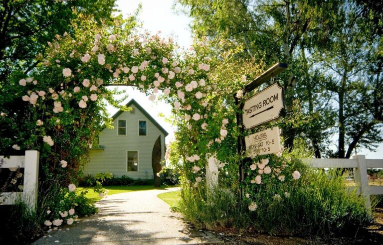 Entrance to Woodward Canyon Winery tasting room with a floral archway and sign displaying hours.